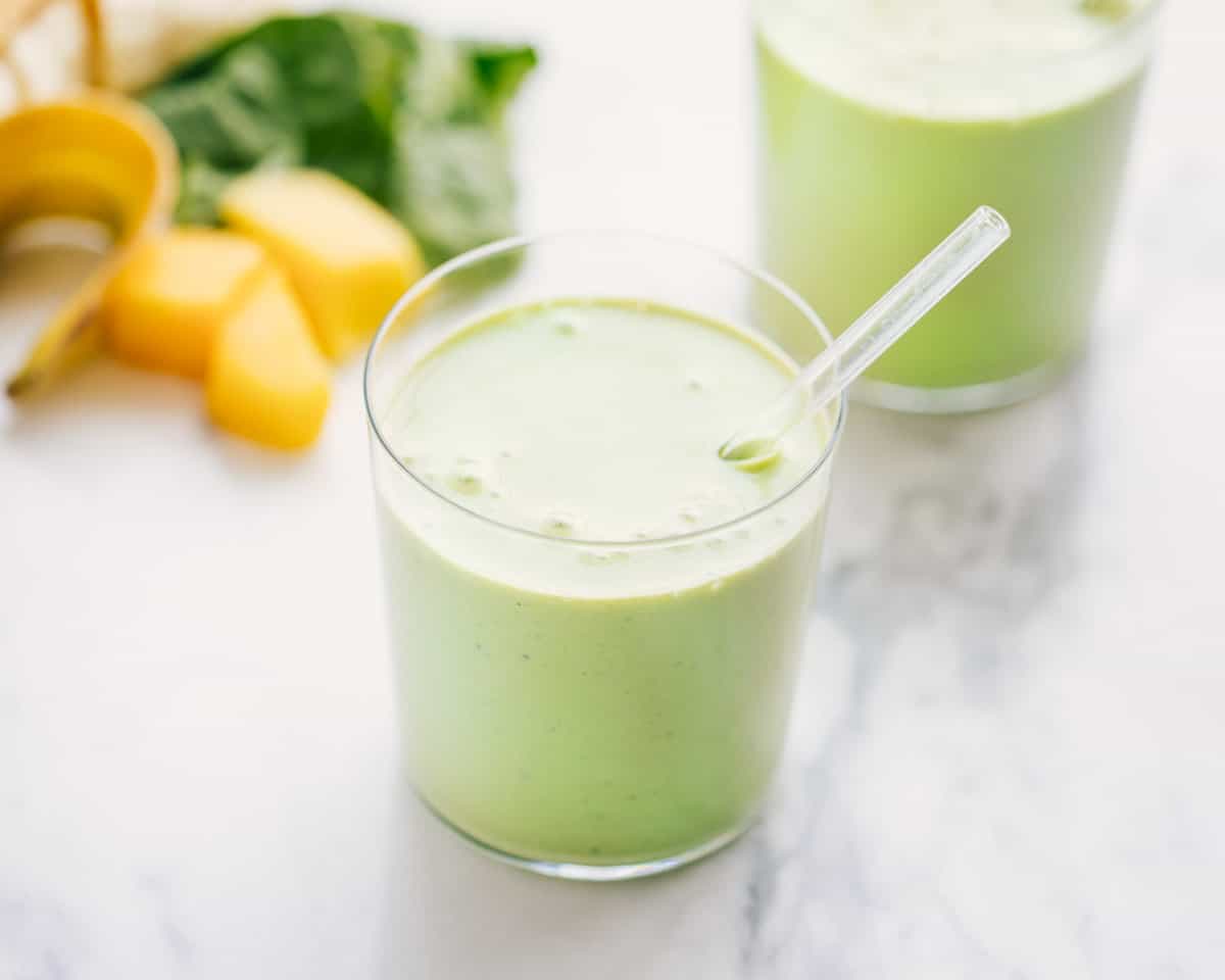 Green smoothie in a clear glass with a clear plastic straw in it. 