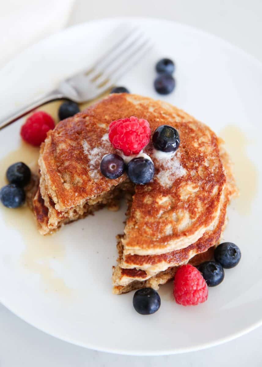 Stack of oatmeal blender pancakes served with berries and maple syrup.