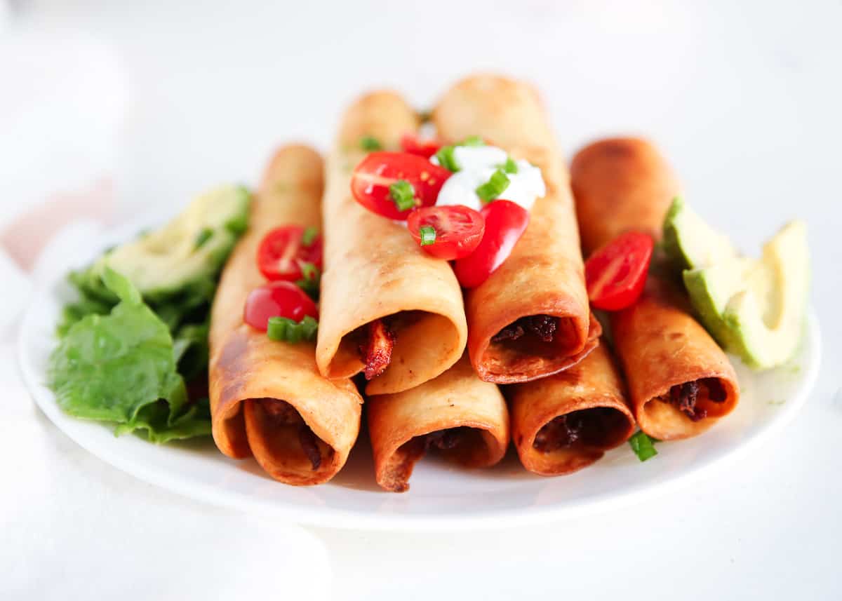 Chicken flautas on a plate with tomatoes.