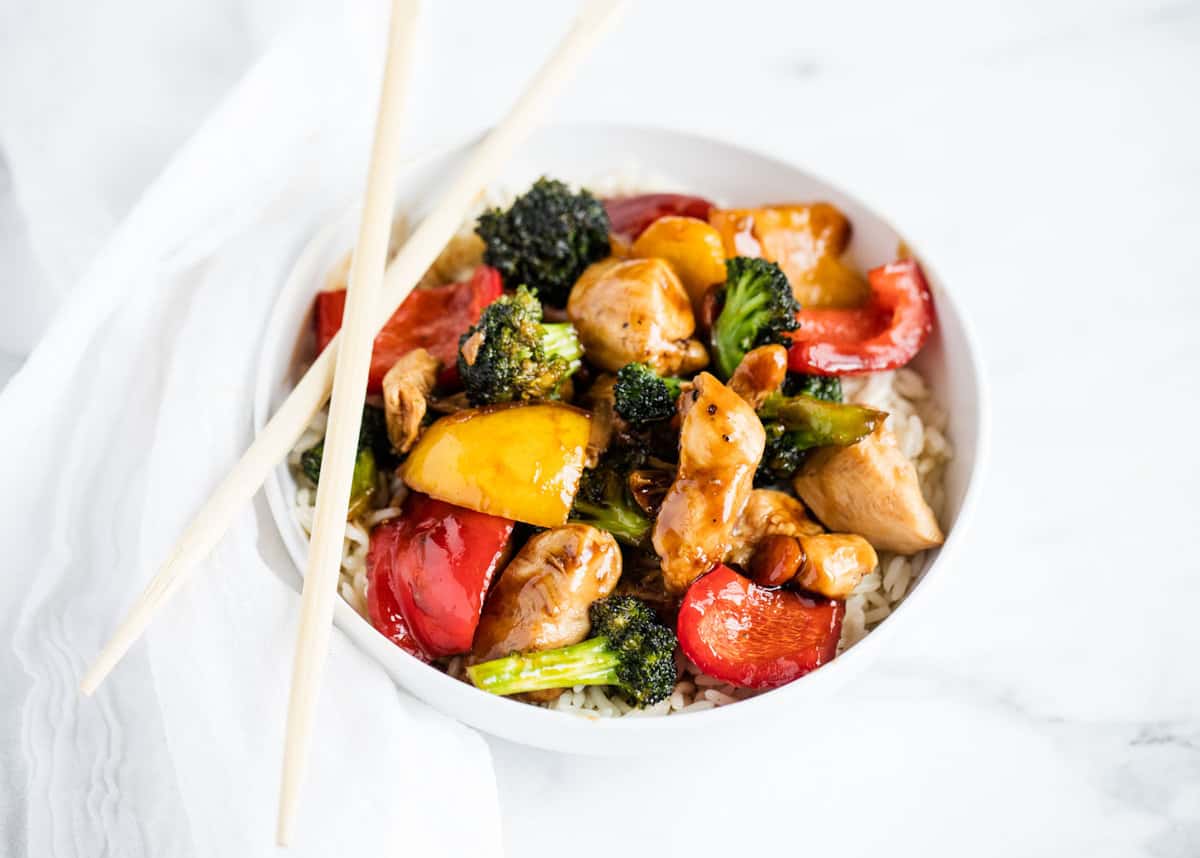 Chicken stir fry in a white bowl with chopsticks on top. 