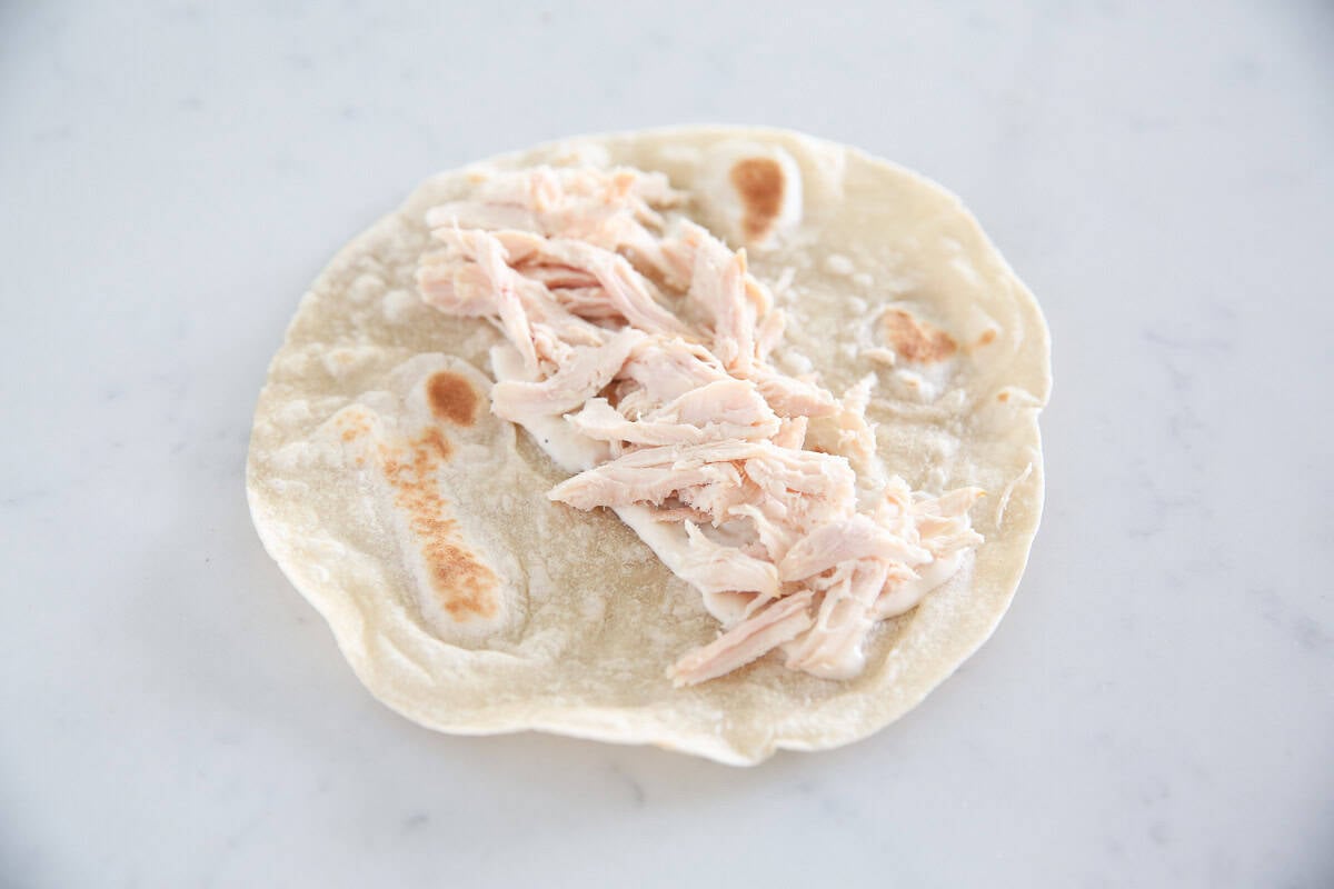 Shredded rotisserie chicken added to a flatbread with Caesar dressing for a chicken Caesar wrap.
