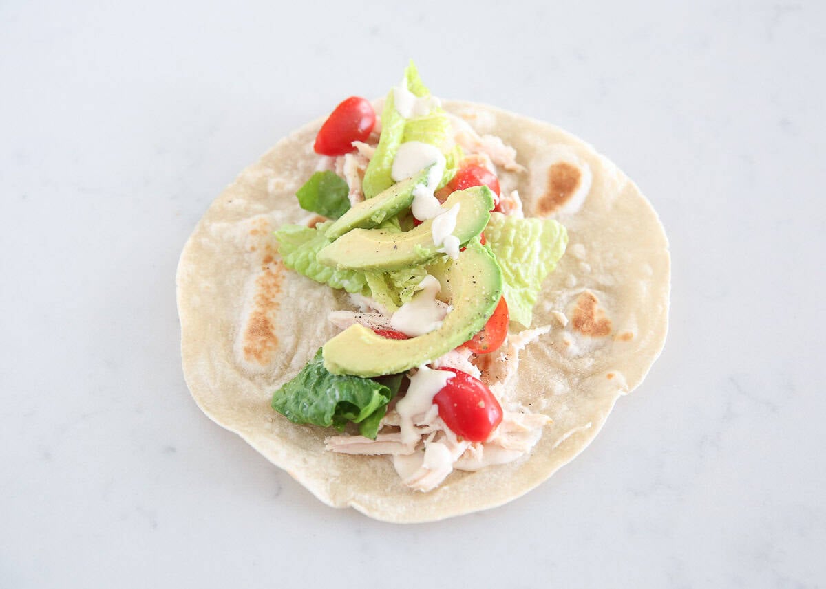 Chicken Caesar wrap filling on a flatbread with romaine, avocado slices, cherry tomatoes, and Caesar dressing.