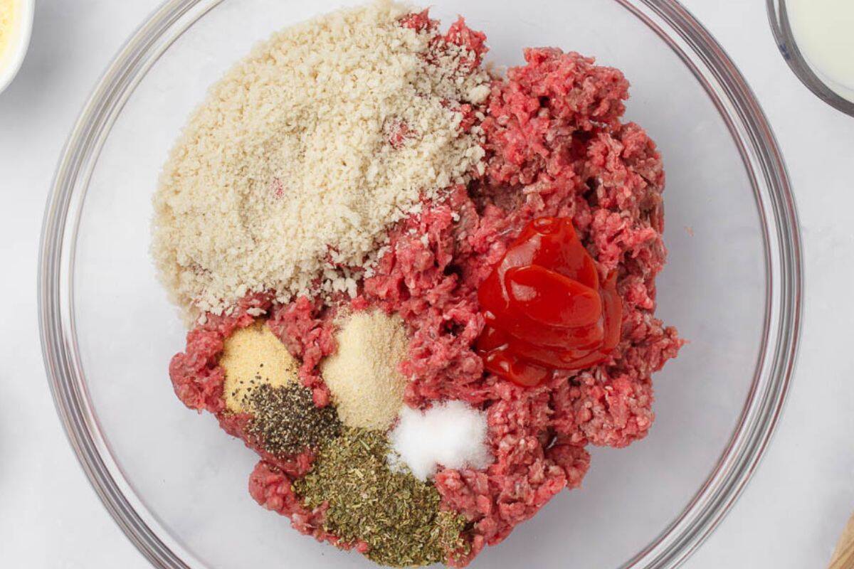 Ground beef mixed with breadcrumbs, seasonings, and ketchup in a glass bowl for mini meatloaf muffins.