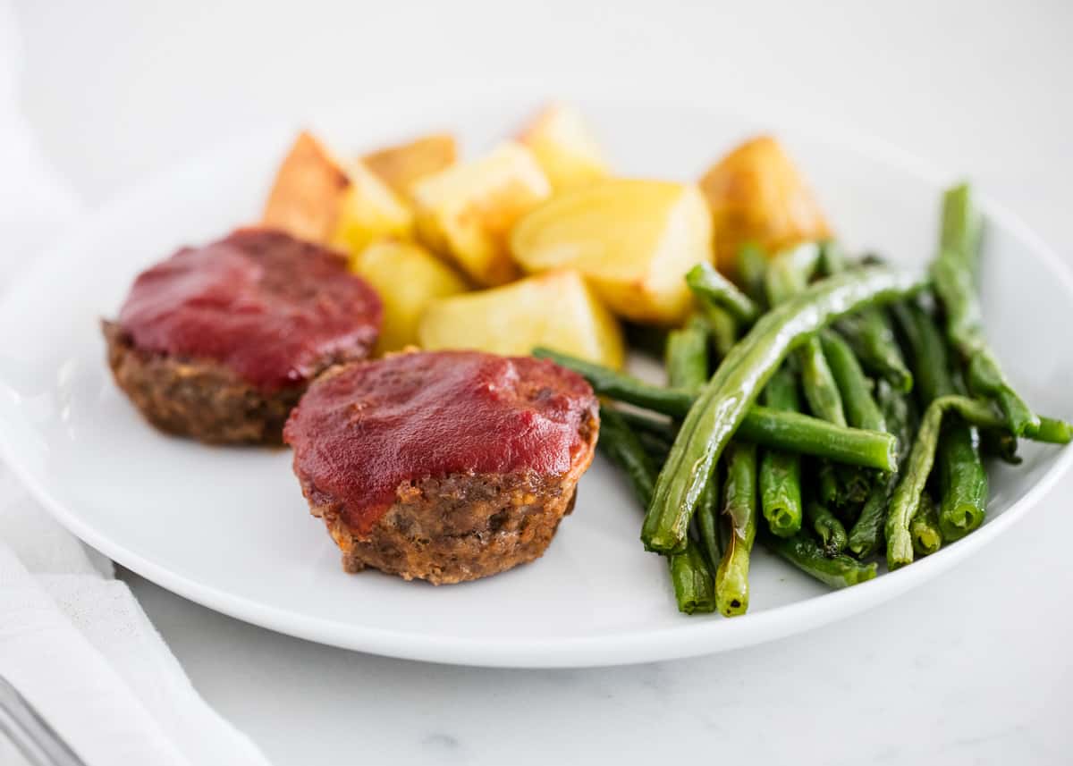 Juicy and tender mini meatloaf muffins coated in a sweet and tangy sauce. An easy, kid-friendly dinner idea that's on the table in just 35 minutes! Meatloaf muffins on a white plate.