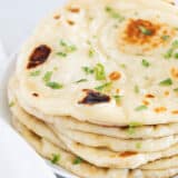 Naan bread stacked on white plate.