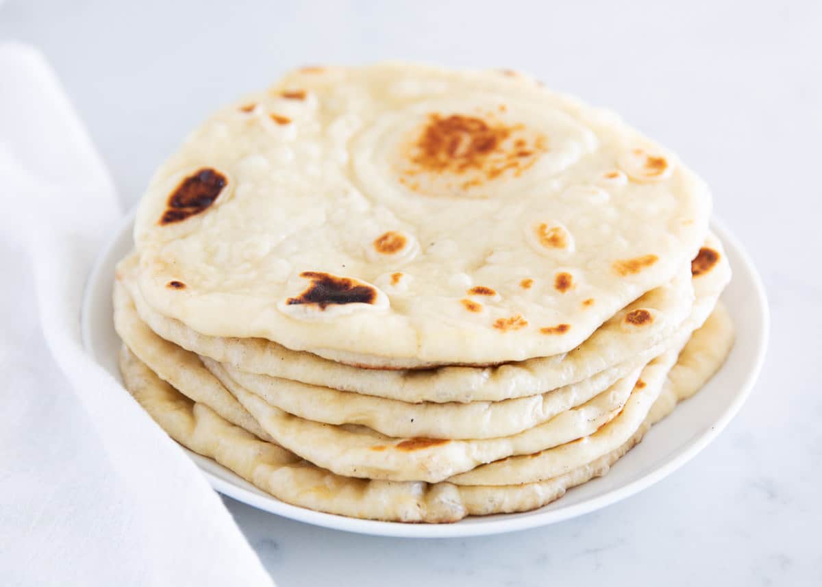 Naan bread stacked on a white plate.