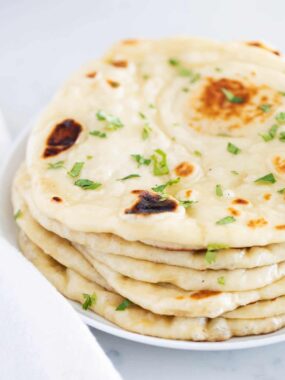 Stack of homemade naan bread garnished with fresh herbs.