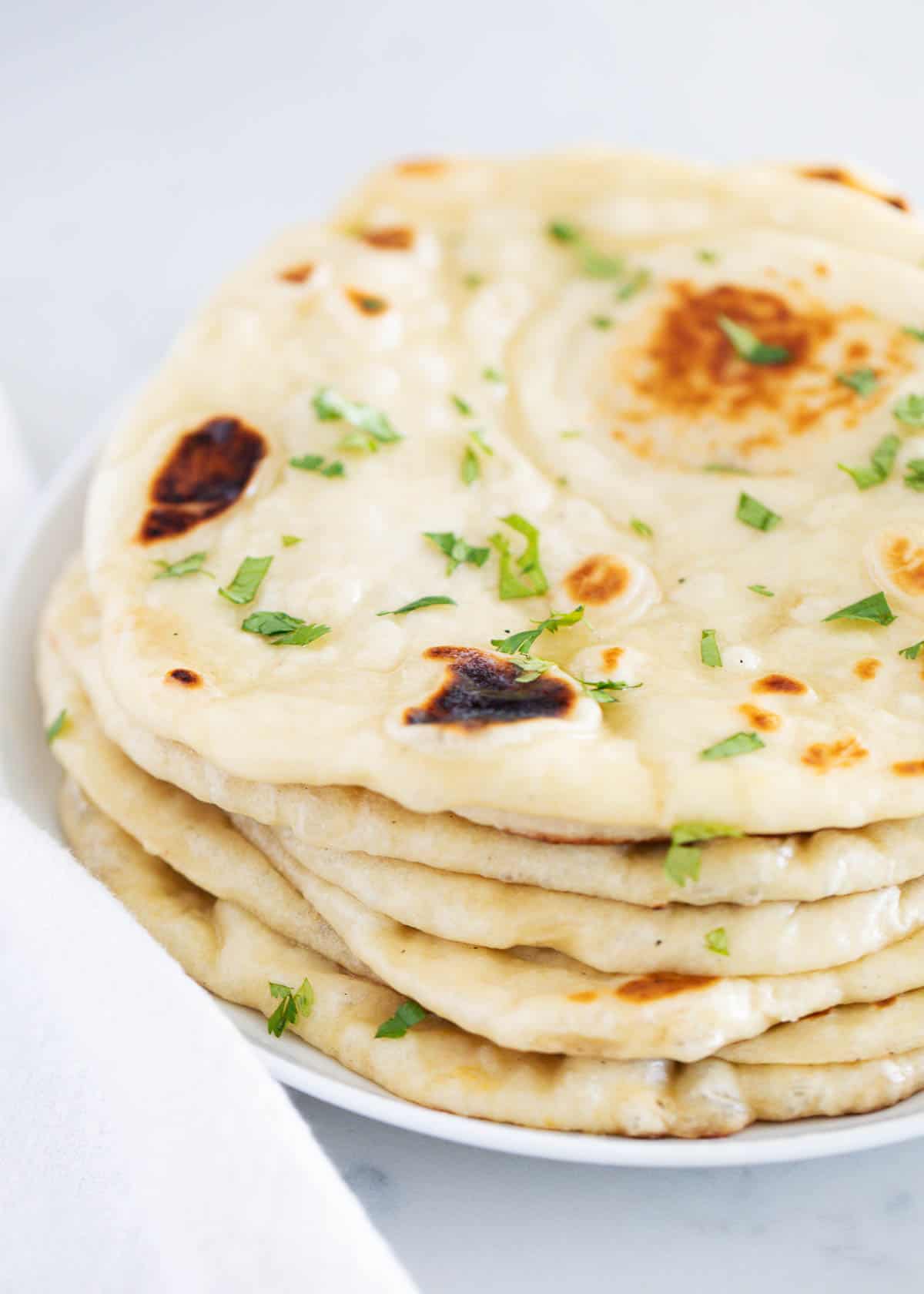 Naan bread stacked on white plate.