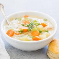 Chicken pot pie soup in a bowl with a biscuit on the side for serving.