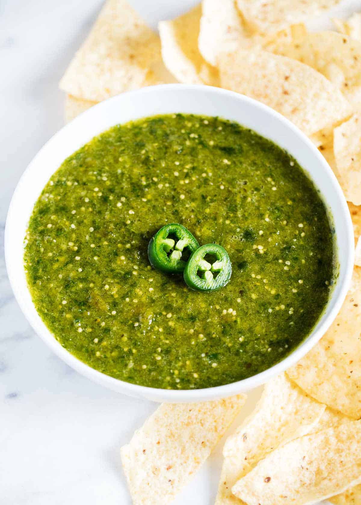 An overhead shot of salsa verde in a white bowl with chips on the side. 