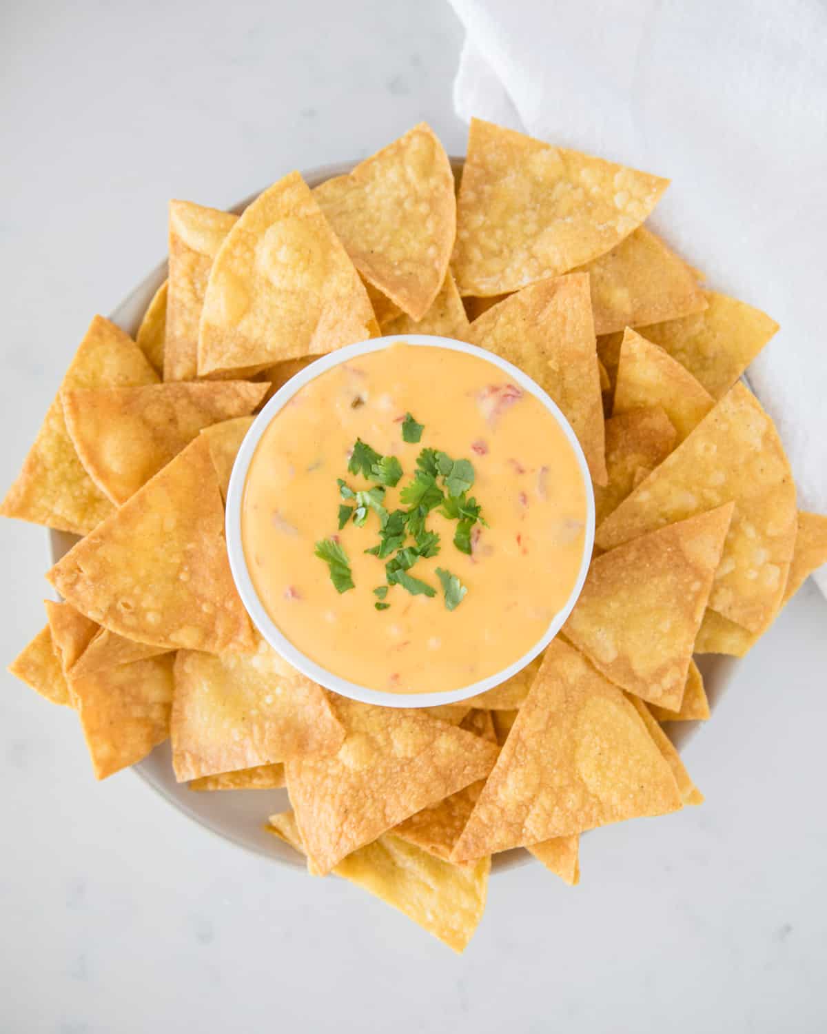 This EASY 2-ingredient Velveeta queso is the perfect last minute dip that's easily made in the microwave or crockpot. It's great for a crowd and tastes super creamy and delicious. Overhead shot of a bowl full of Velveeta queso dip recipe on a platter with tortilla chips.