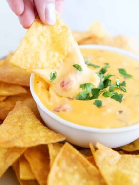 A close up of dipping a chip into Velveeta queso.
