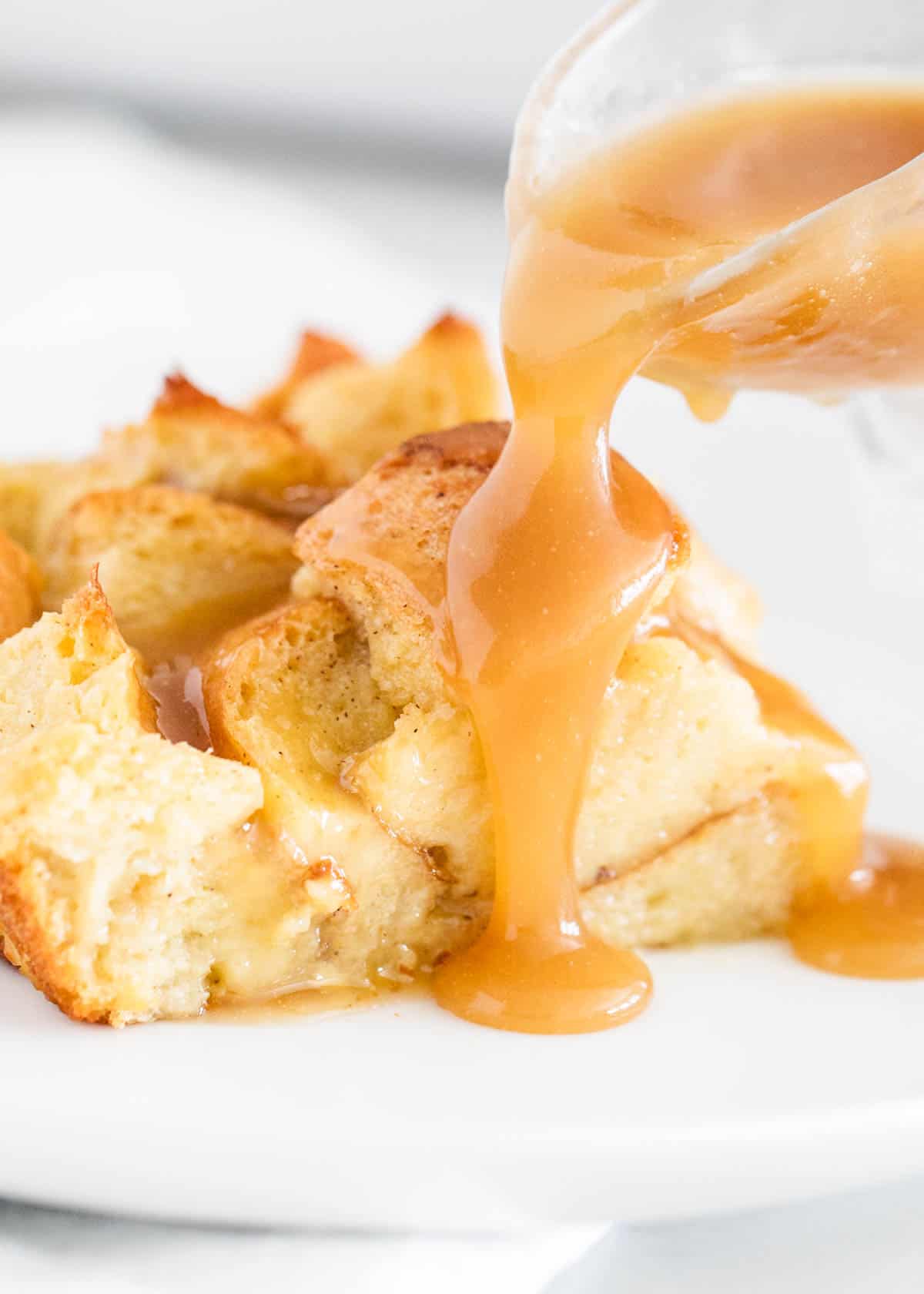 Up close photo of bread budding sauce being drizzled over top bread pudding. 