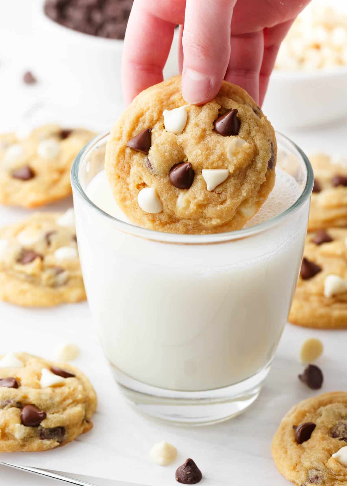 A chocolate chip pudding cookie being dunked into a glass of milk.