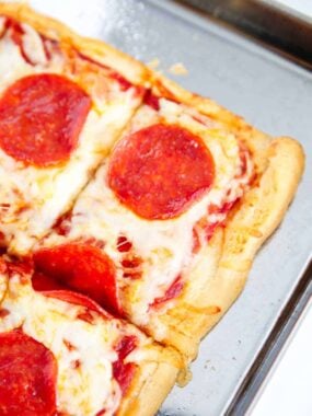 Sliced crescent roll pizza on a metal baking sheet.