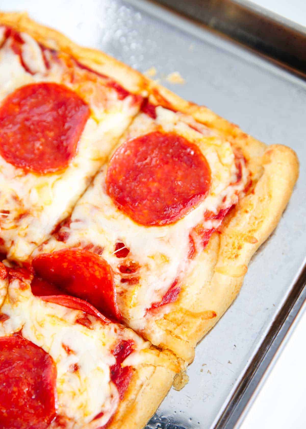 Sliced crescent roll pizza on a metal baking sheet.