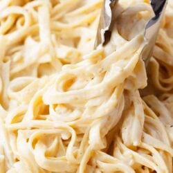 Twirling fettuccine alfredo with tongs.