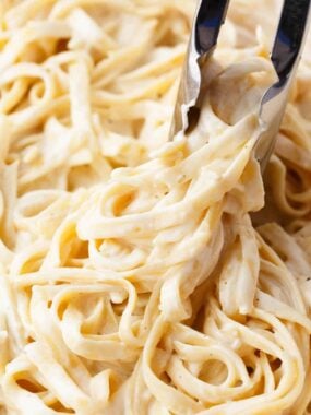 Twirling fettuccine alfredo with tongs.