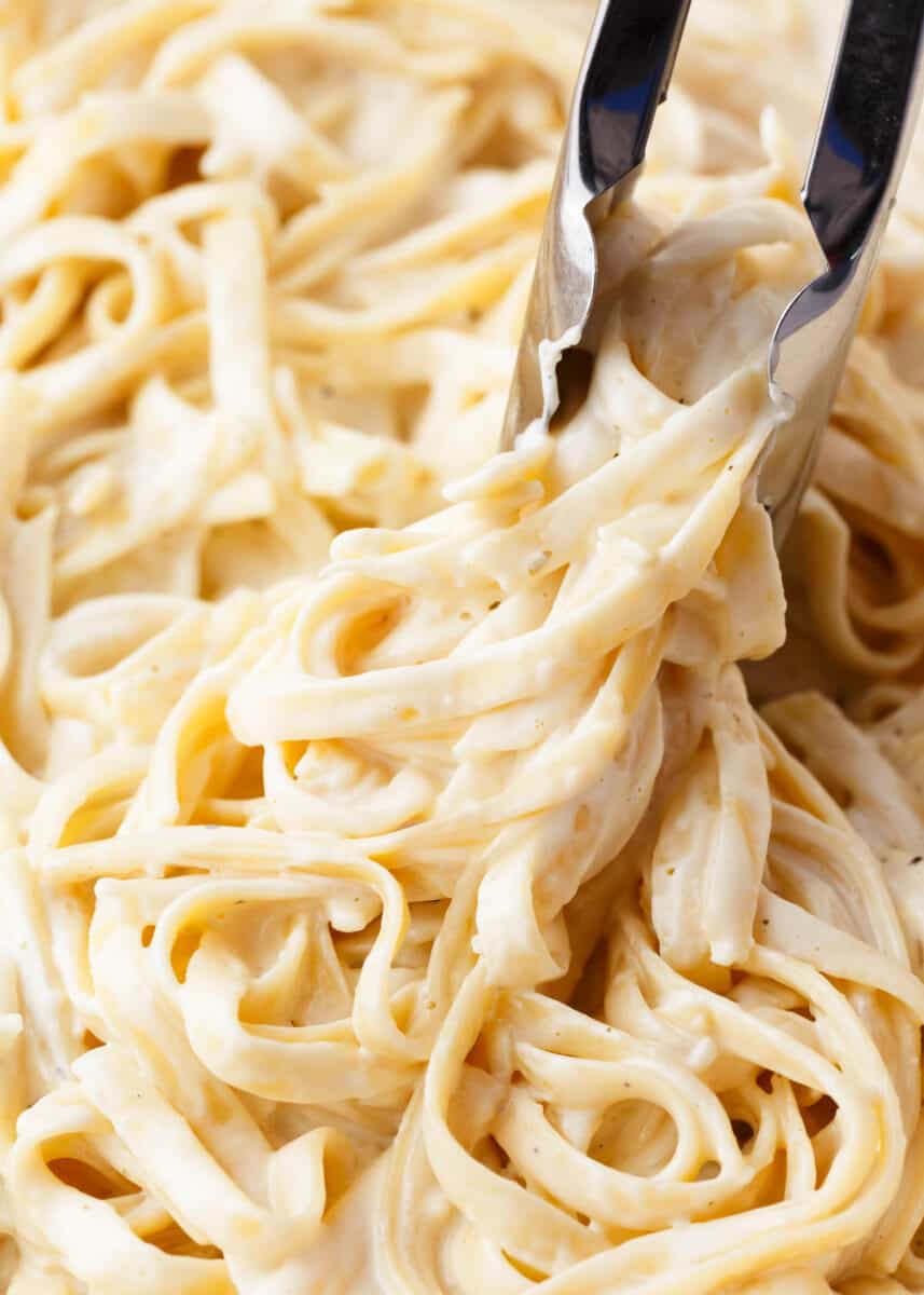 Twirling fettuccine alfredo with tongs.