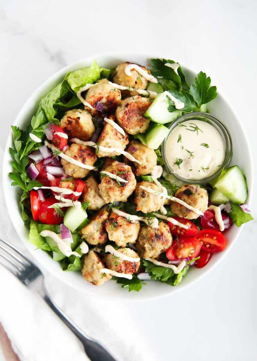 Greek meatballs in a bowl of lettuce with tomatoes and sauce. 