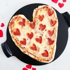 A heart shaped pizza recipe on a baking stone with extra Valentine's heart decor on counter.