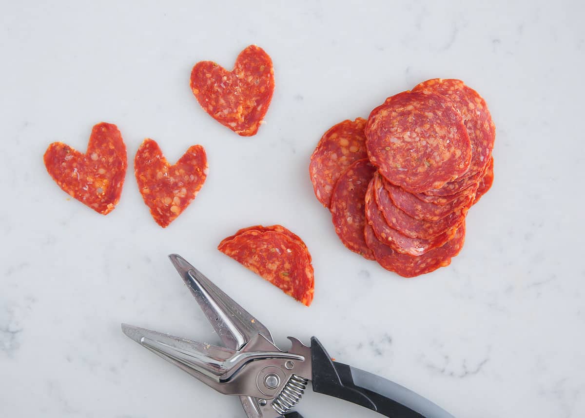 Using kitchen cutters to cut pepperoni into heart shapes.