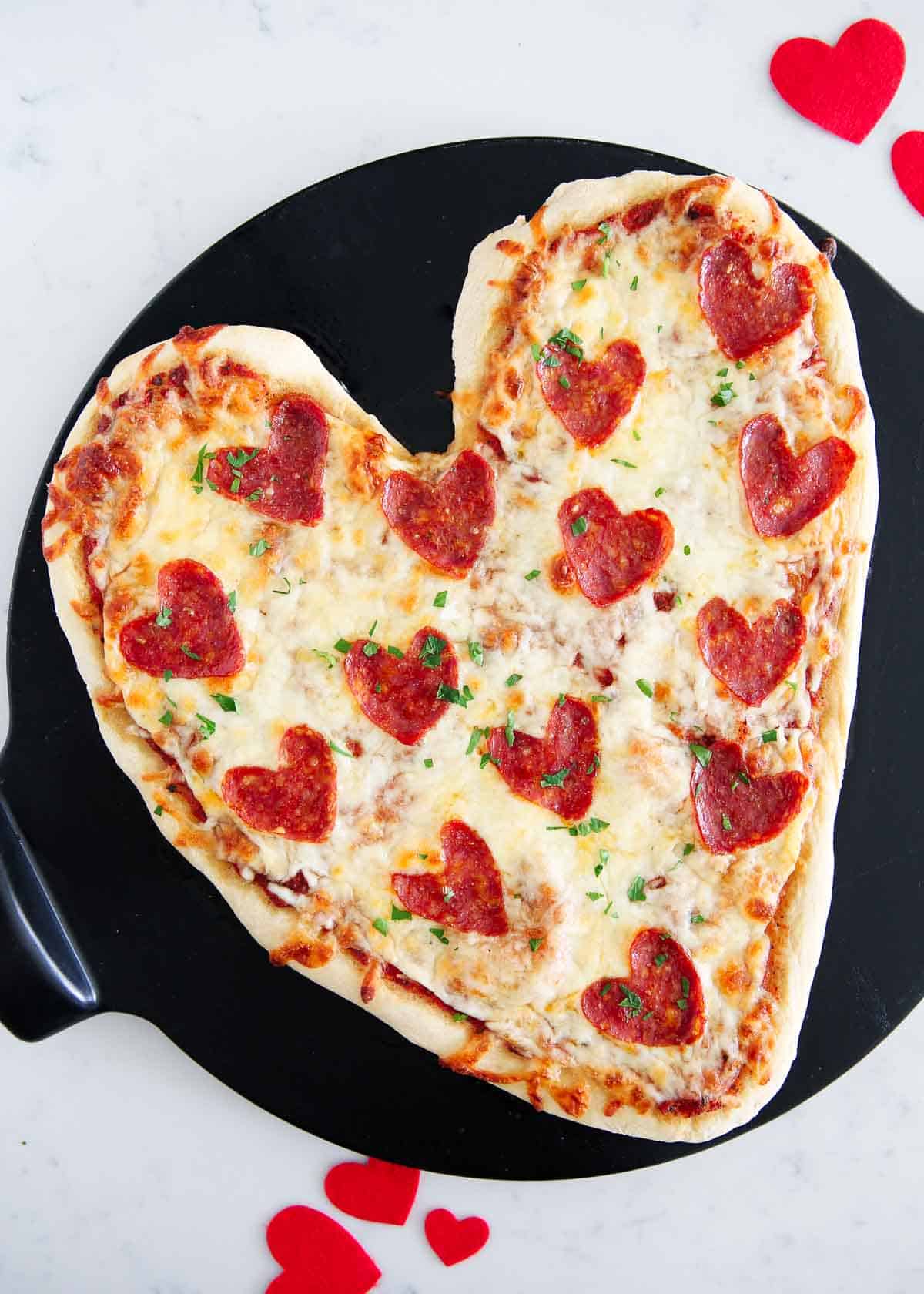 Heart shaped pizza on pizza stone.