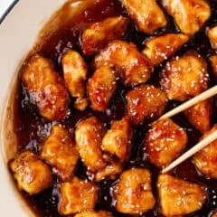 Crispy honey sesame chicken coated in a thick, glossy sauce and sprinkled with sesame seeds in a skillet.