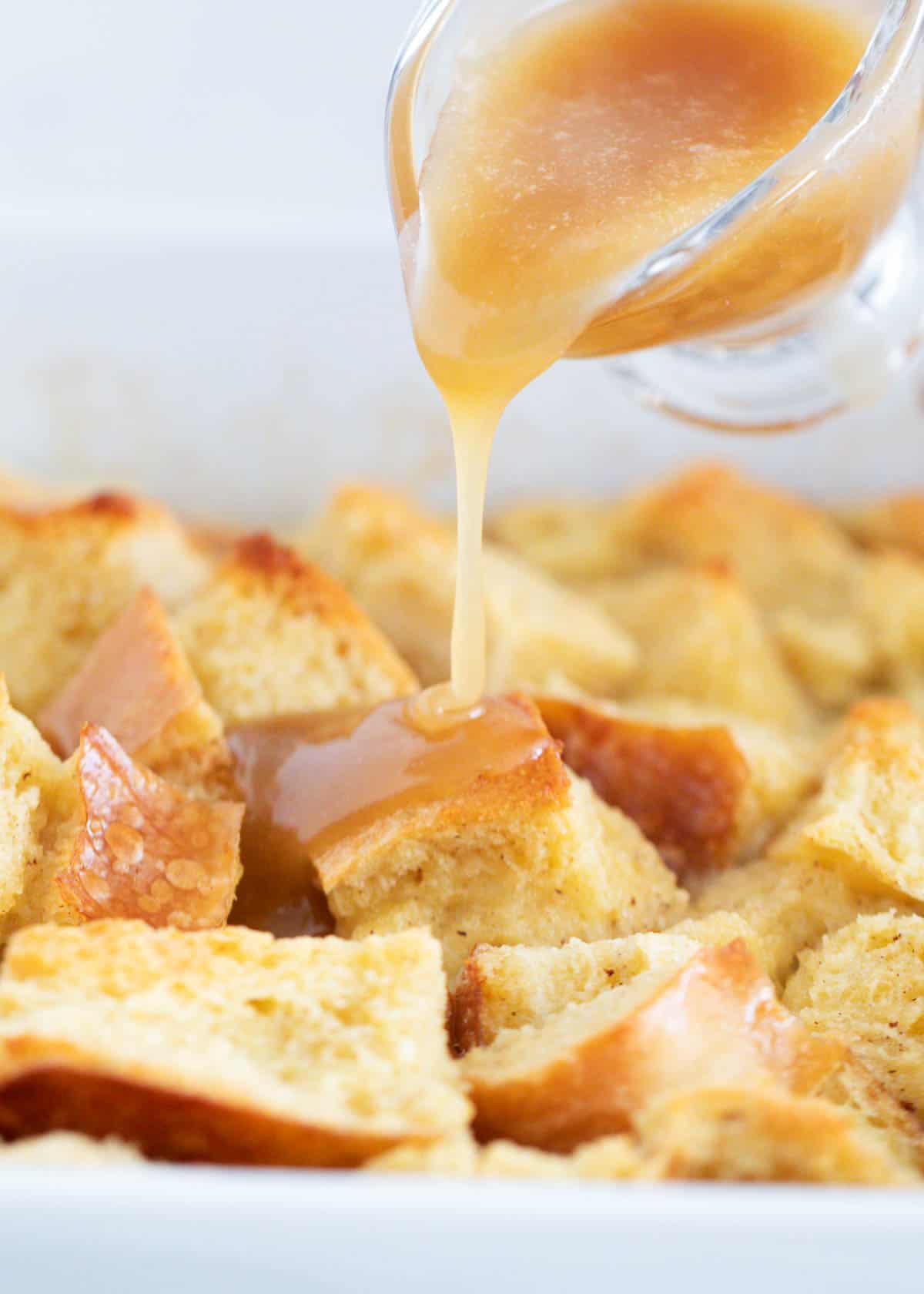 Pouring bread pudding sauce over top bread pudding. 