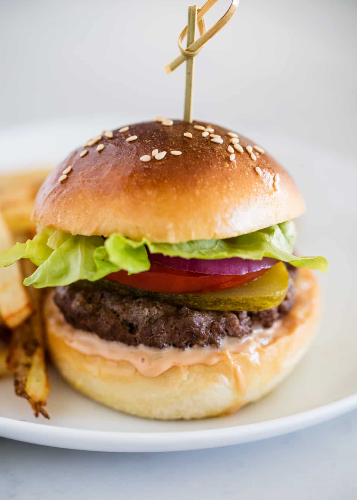 Baked hamburger on a white plate with fries.