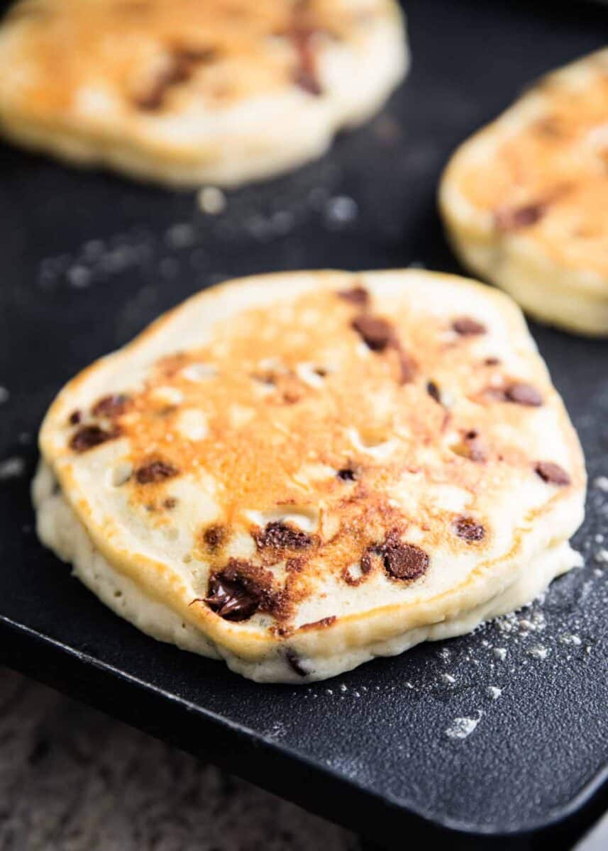 Chocolate chip pancakes cooking on griddle.