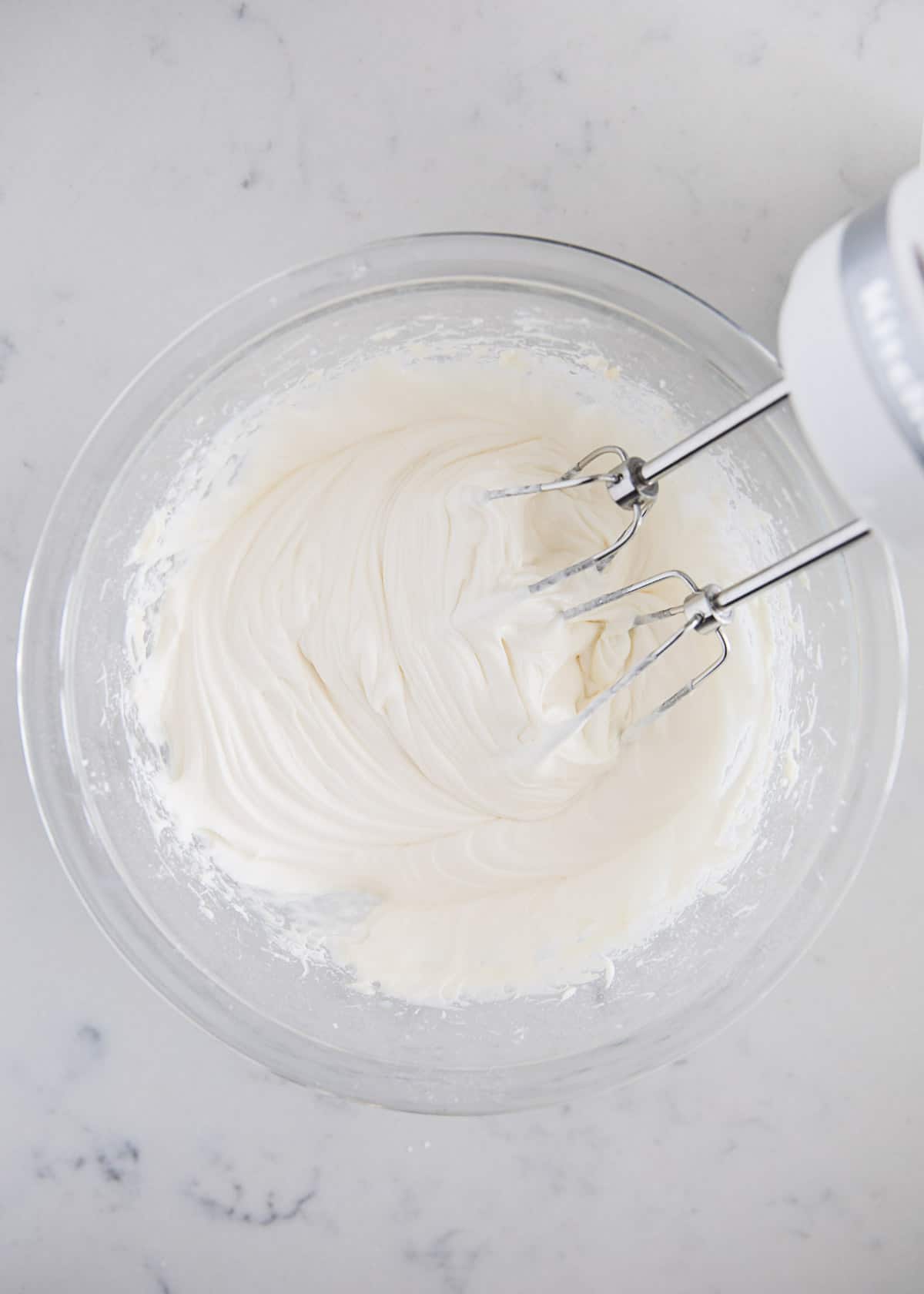 Electric mixer in a glass bowl making cream cheese glaze. 