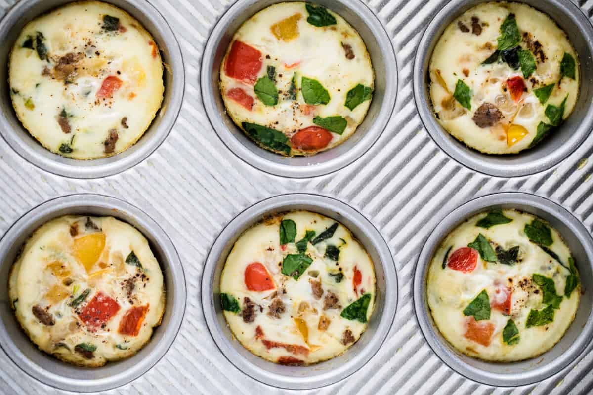 Six muffins with vegetables and cheese in muffin tins. 