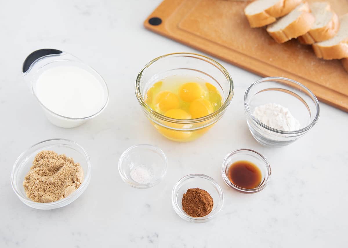 French bread on cutting board, eggs, milk, brown sugar, powdered sugar, salt, cinnamon and vanilla extract.