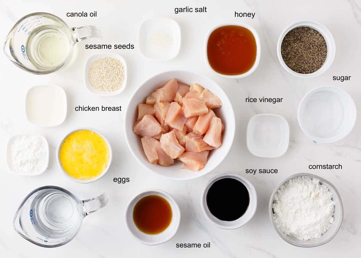 Overhead view of honey sesame chicken ingredients, including cubed chicken breast, honey, soy sauce, sesame seeds, cornstarch, eggs and oil.