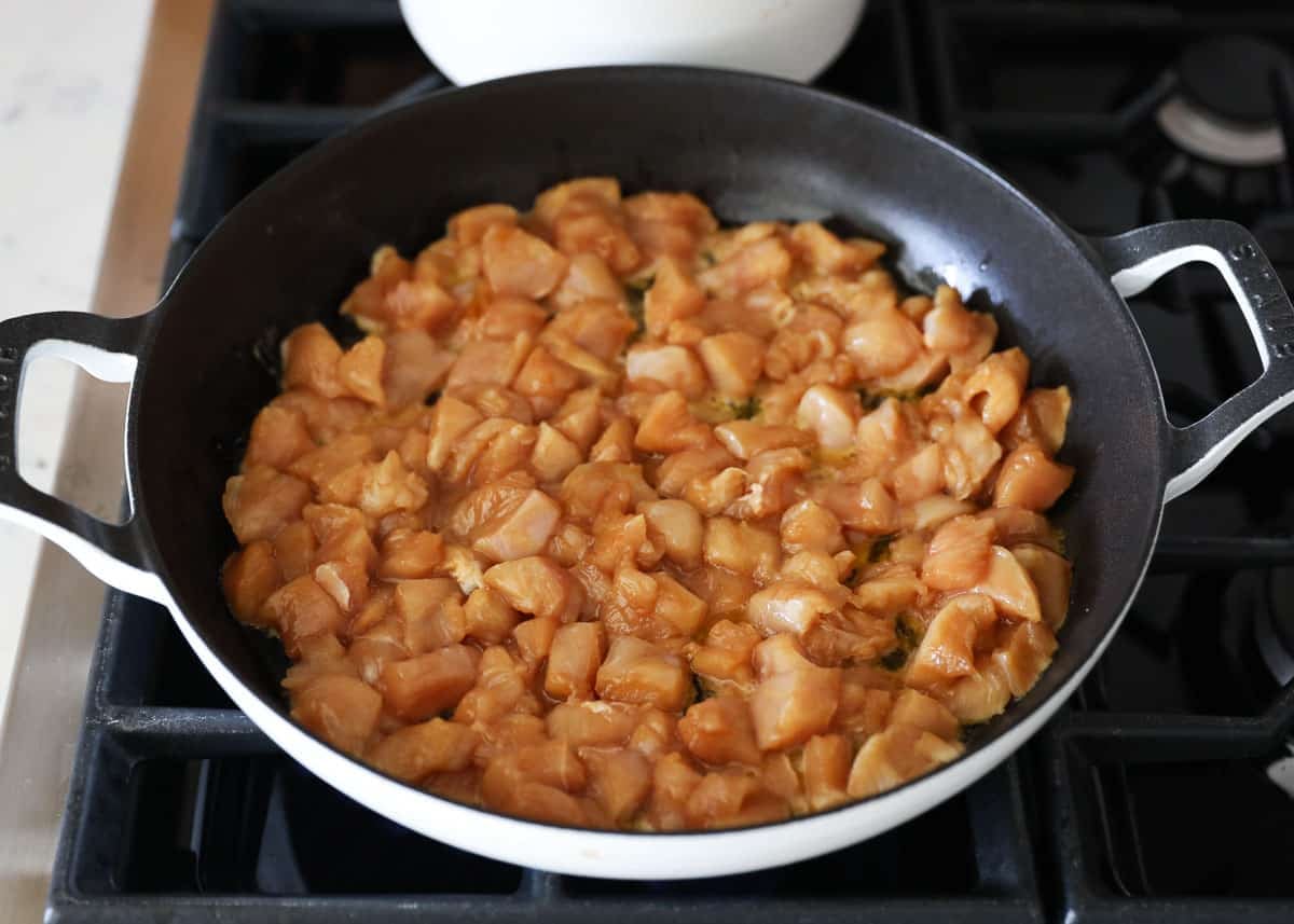 Marinated diced chicken in a white skillet ready to cook.