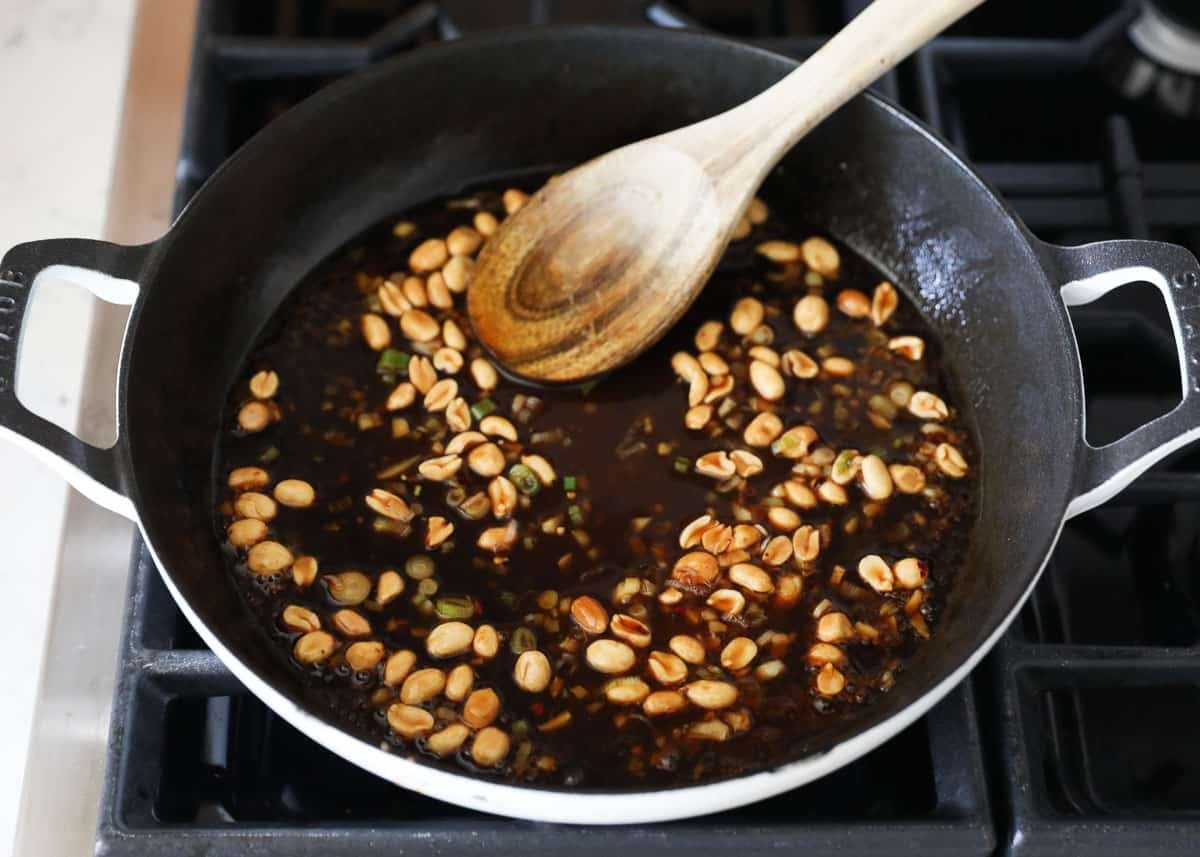 Kung pao sauce simmering in a skillet with peanuts and sliced green onions.