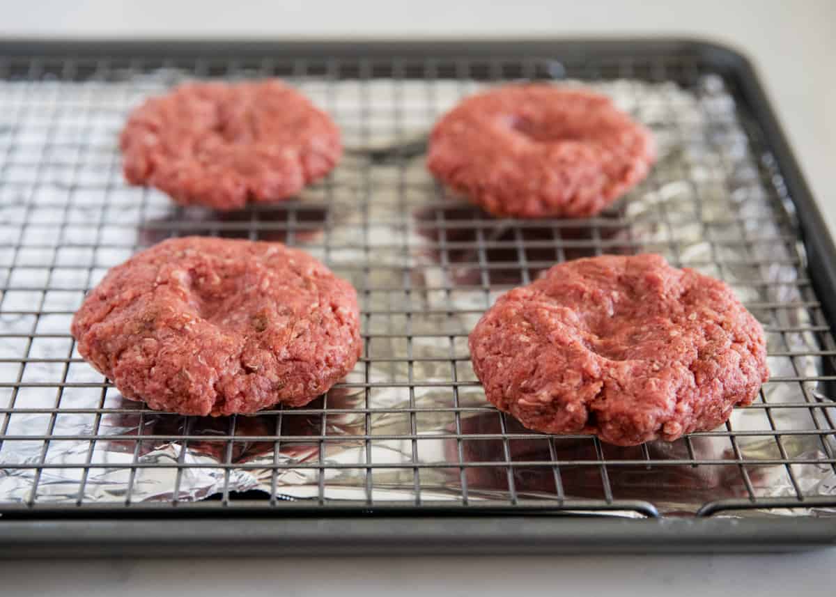 Burger patties on a cooling rack with baking sheet. 