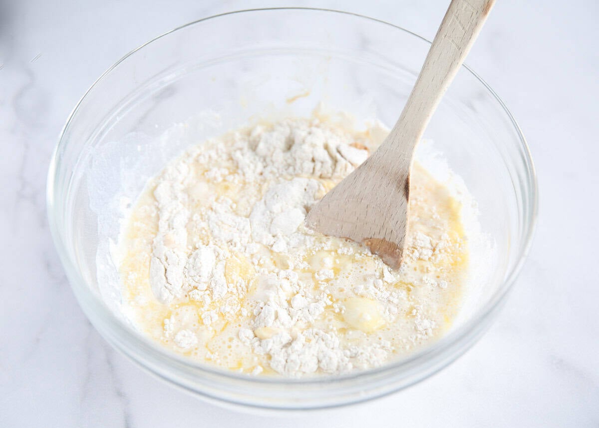 Dry and wet ingredients combining in a glass bowl with a wooden spoon to make buttermilk chocolate chip pancakes.