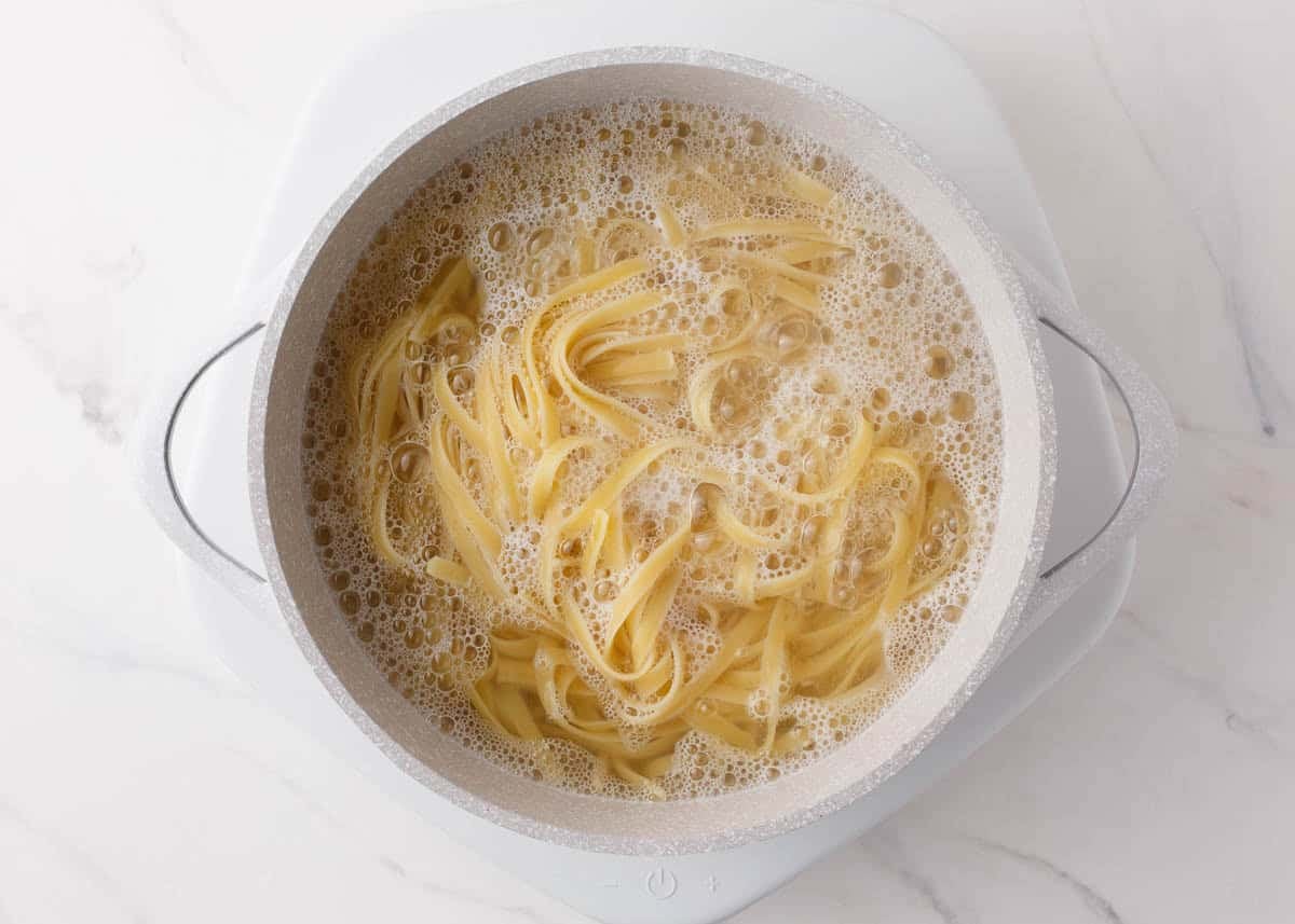 Fettuccine noodles boiling in a large white pot.