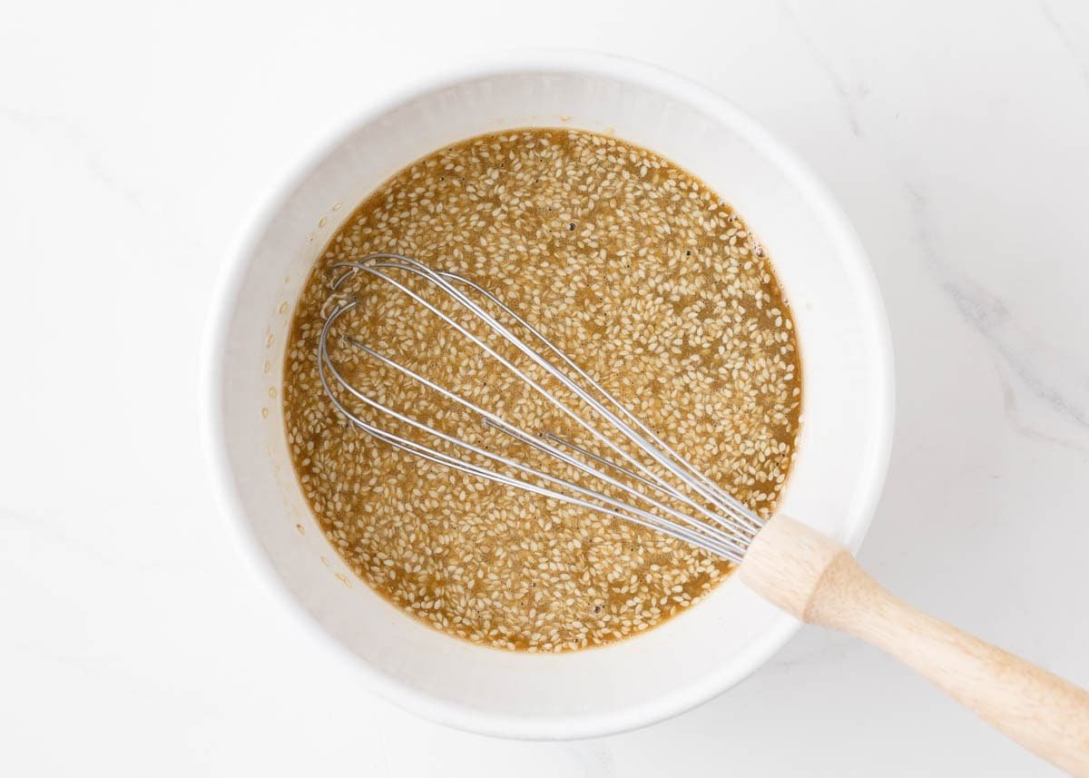 Honey sesame sauce in a bowl with a whisk.