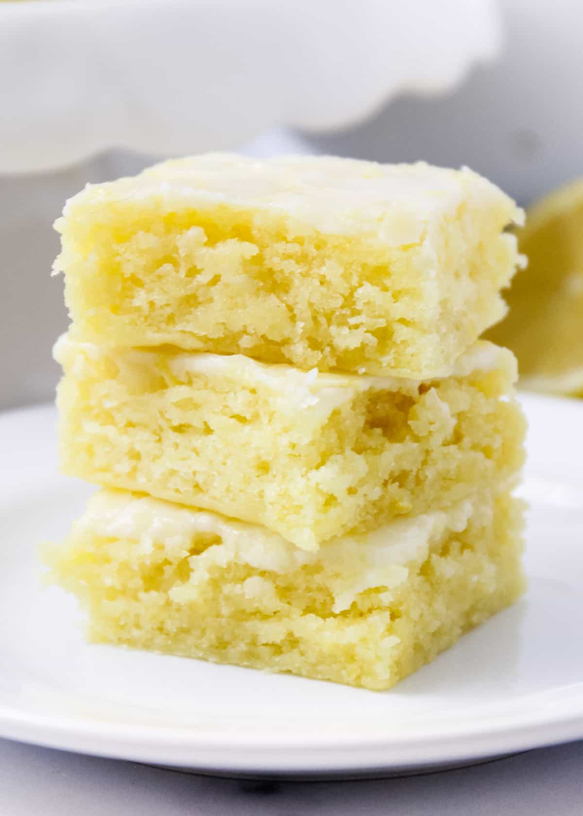 Lemon brownies stacked three high on a white plate. 