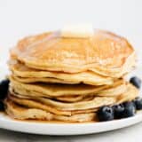 Stack of ricotta pancakes on white plate with blueberries.
