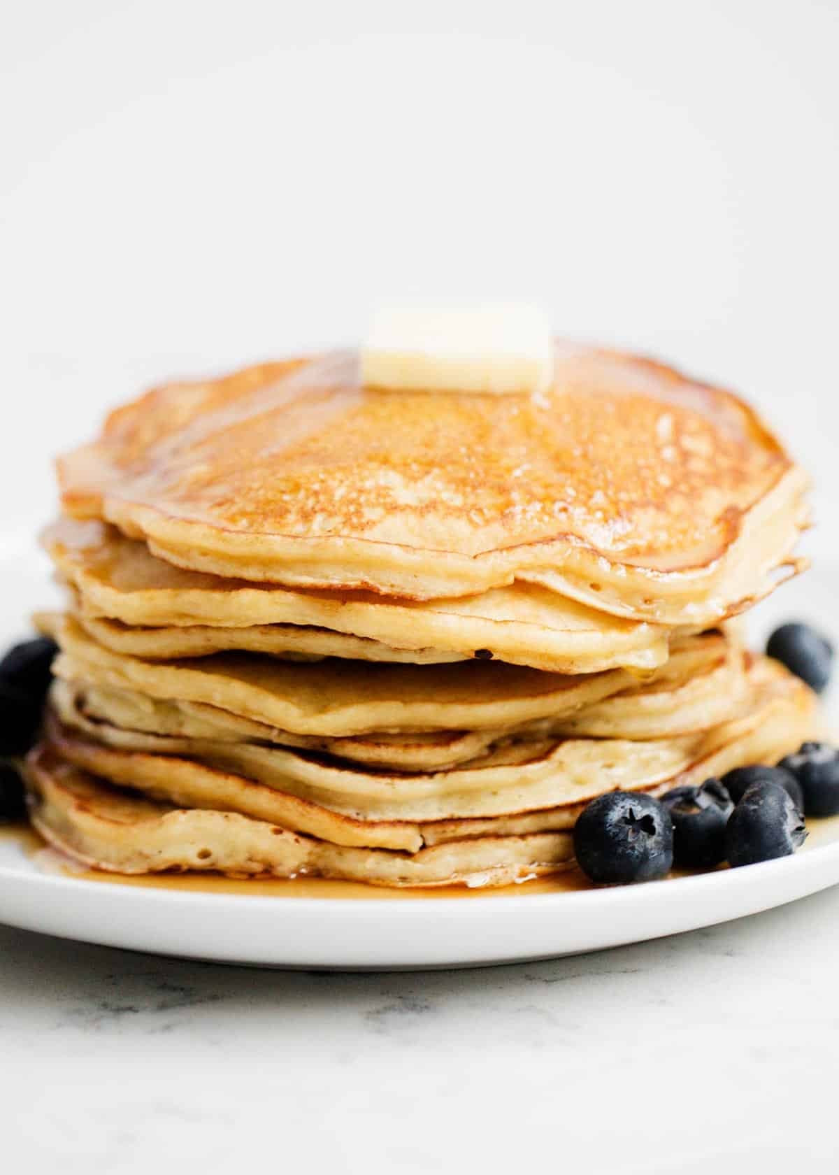 Stack of ricotta pancakes on white plate with blueberries.