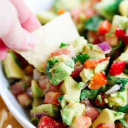 Scooping avocado salsa with a tortilla chip.