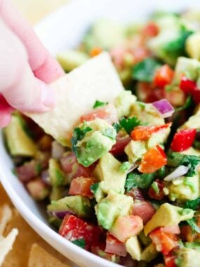 Scooping avocado salsa with a tortilla chip.