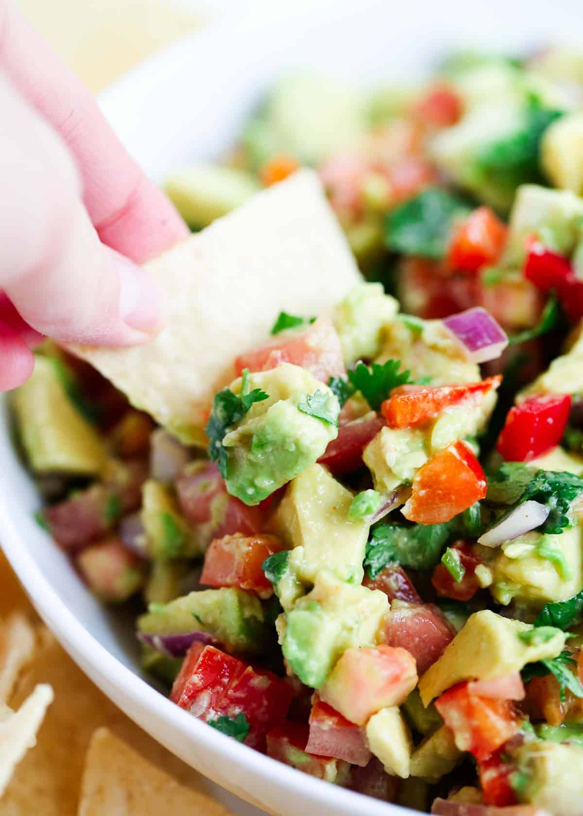 Scooping avocado salsa with a tortilla chip.