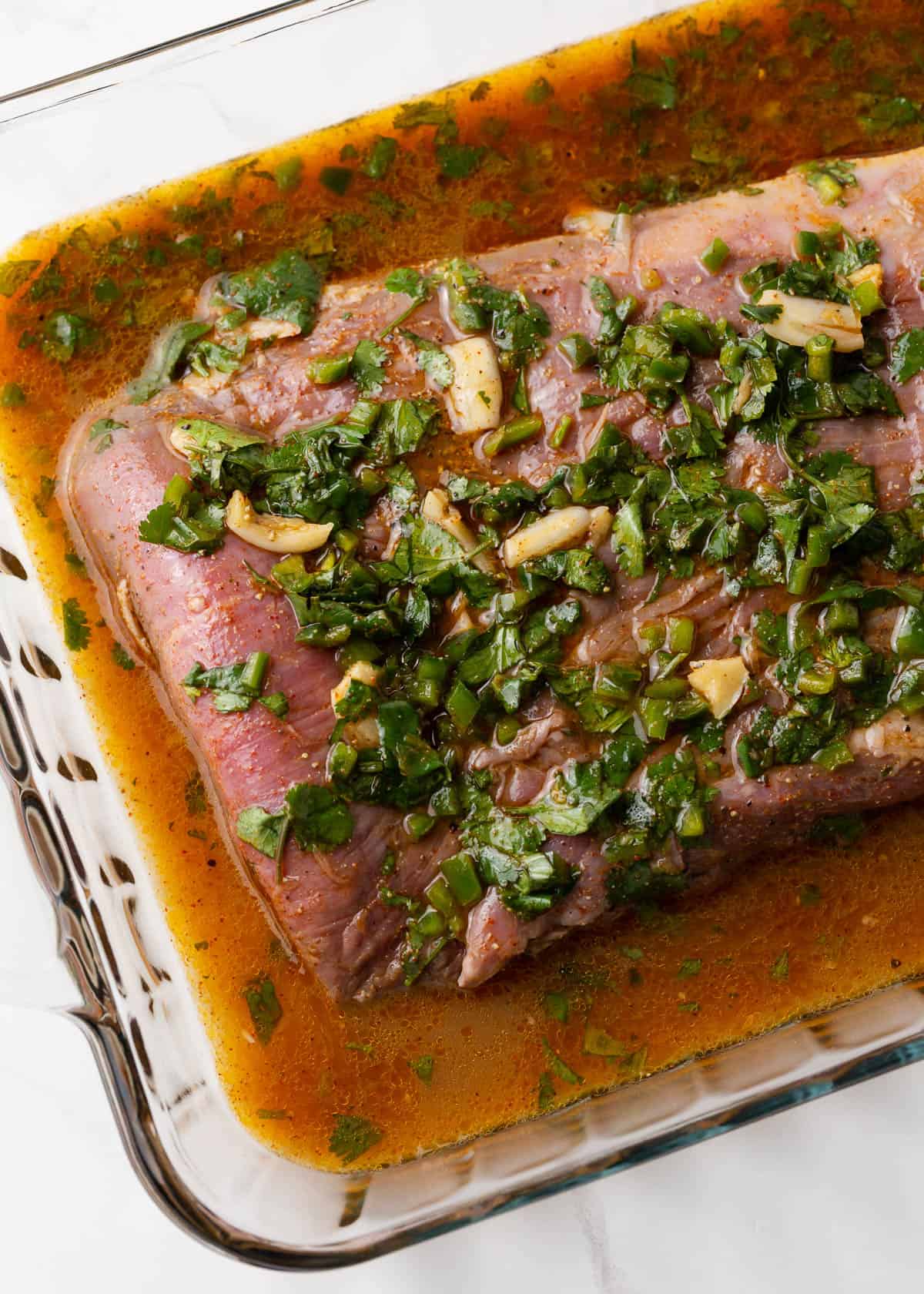 Carne asada marinating in glass dish.