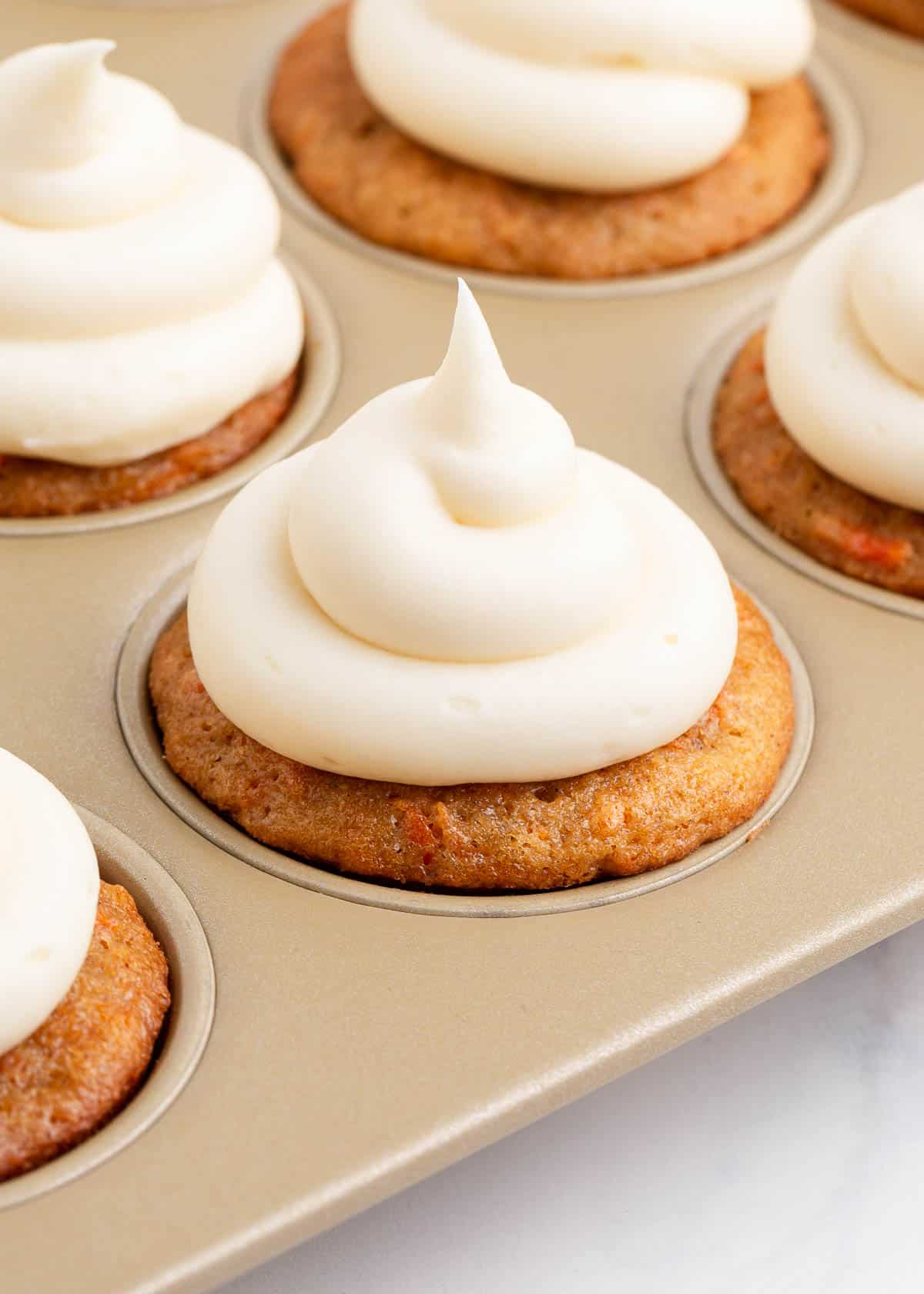 Carrot cake cupcakes in a muffin pan with frosting. 
