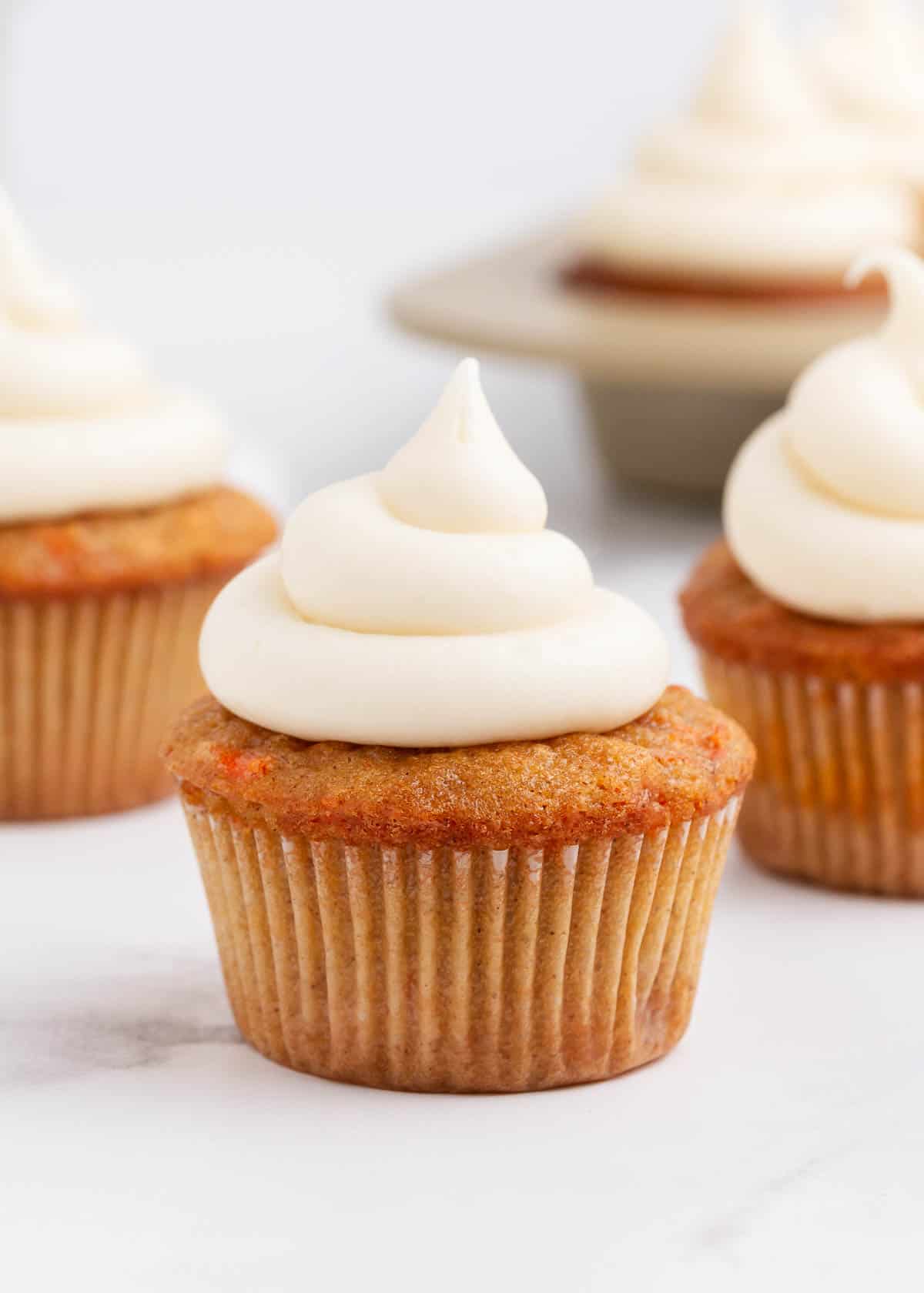 A carrot cake cupcake with frosting on the counter. 